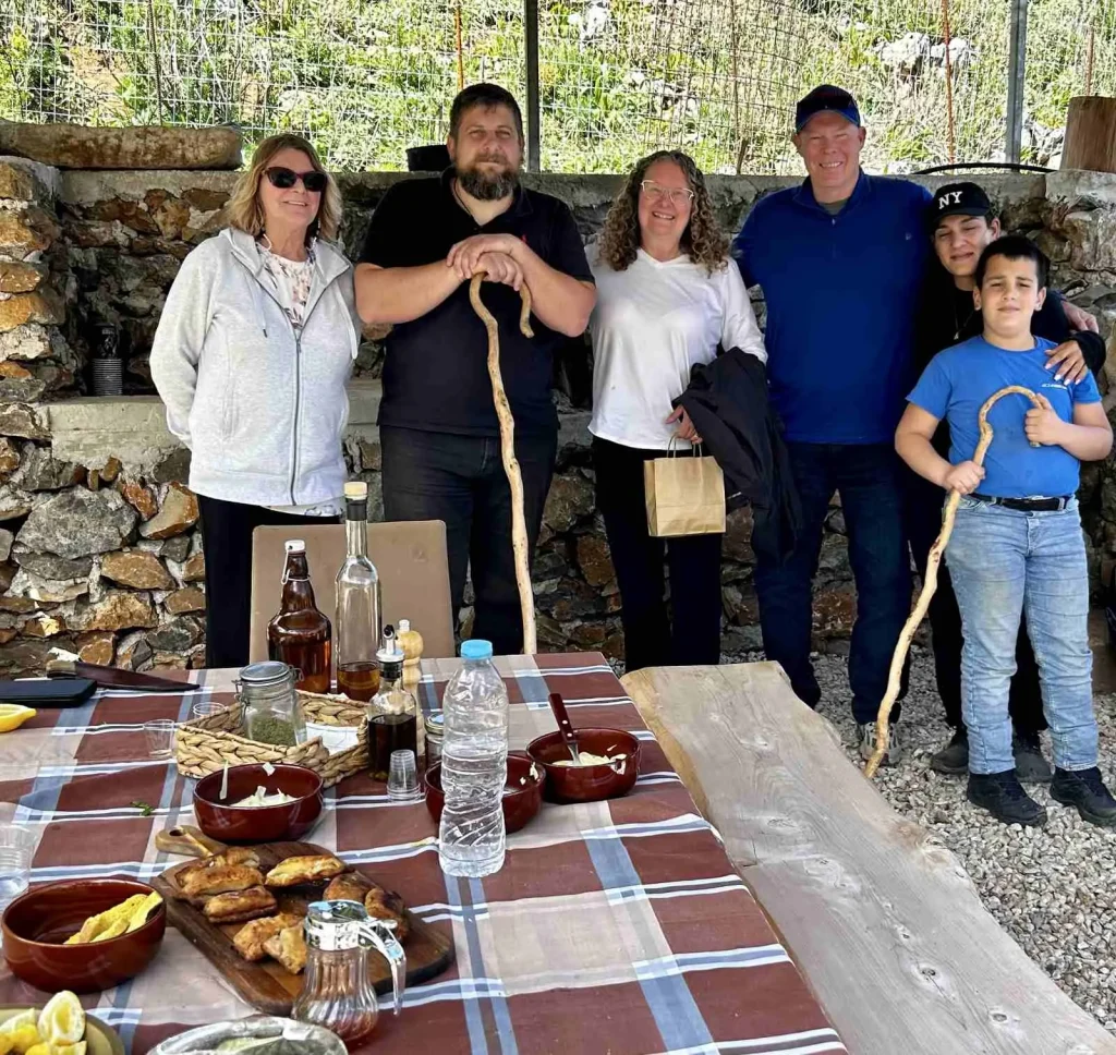 A group of people standing and smiling together behind a table filled with local food and drinks at Arevitis Farm.