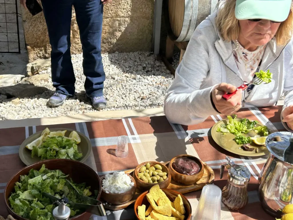 A woman enjoying a traditional farm-to-table Cretan meal at an outdoor table with fresh salad, olives, and local delicacies.