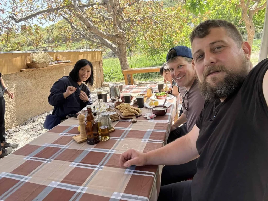 A group of smiling visitors enjoying a traditional Cretan meal outdoors at a long table covered in local delicacies at Arevitis Farm.